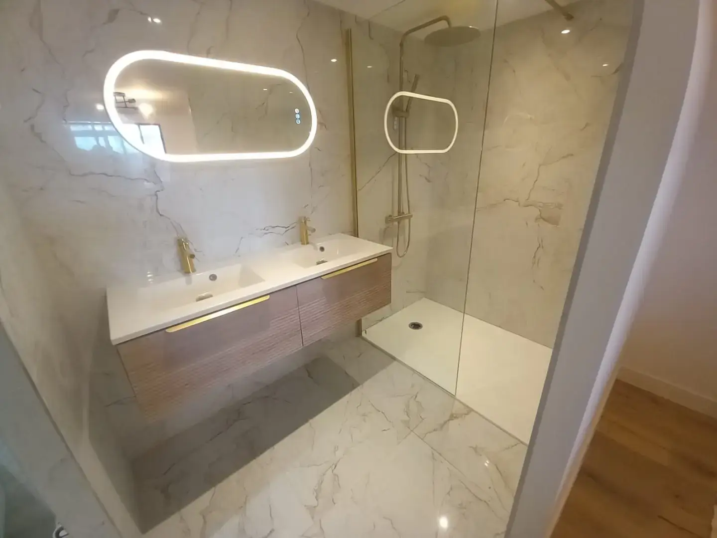 Salle de bain rénovée avec meuble vasque, miroir lumineux et douche vitrée